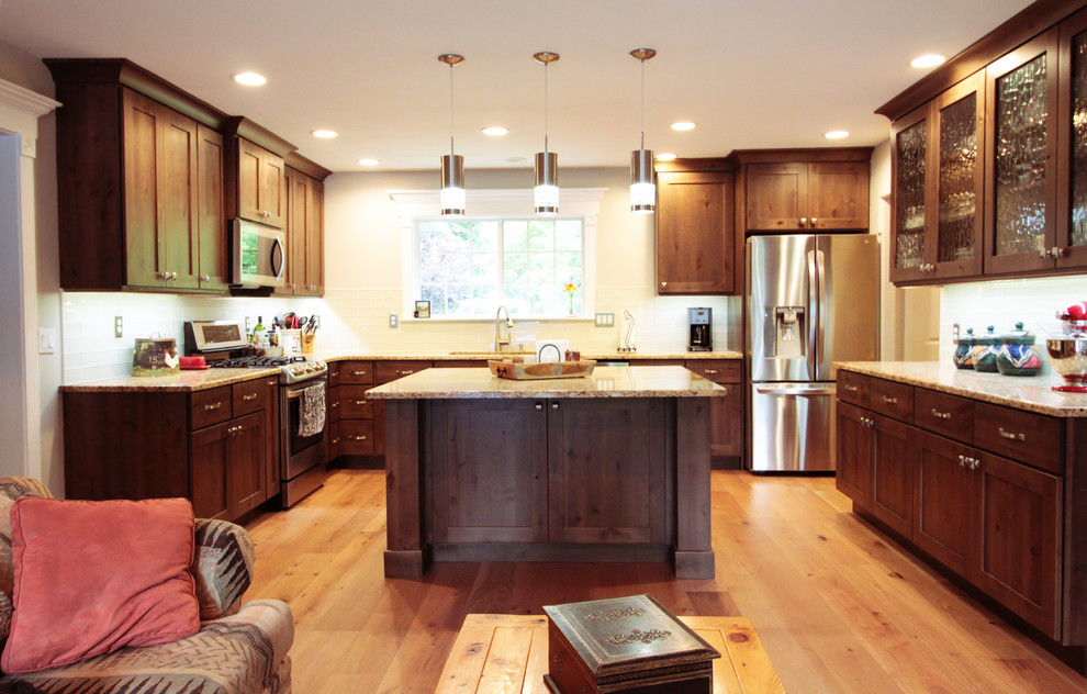 Open concept kitchen - large rustic u-shaped light wood floor and brown floor open concept kitchen idea in Boise with an undermount sink, shaker cabinets, brown cabinets, granite countertops, white backsplash, glass tile backsplash, stainless steel appliances and an island