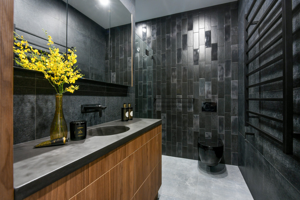 This is an example of a contemporary bathroom in Sydney with flat-panel cabinets, medium wood cabinets, a wall-mount toilet, black tile, an integrated sink, grey floor and grey benchtops.