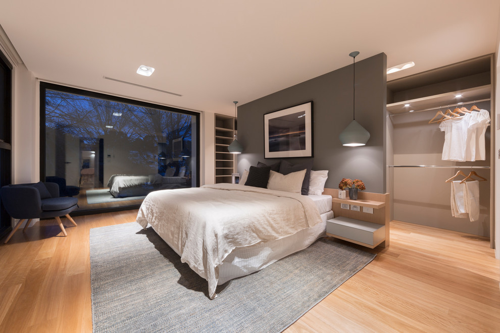 Large contemporary master bedroom in Canberra - Queanbeyan with light hardwood floors.