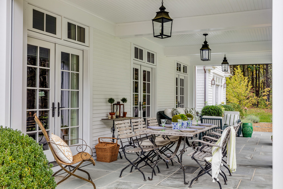 This is an example of a mid-sized farmhouse stone back porch design in Boston with a roof extension.