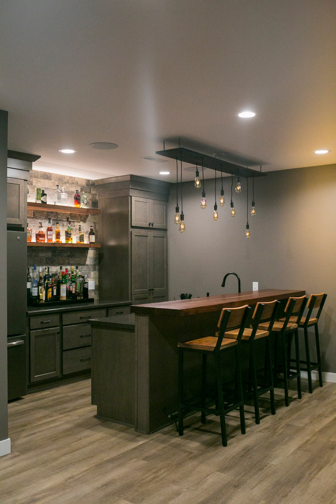 Design ideas for a large arts and crafts galley seated home bar in Other with a drop-in sink, recessed-panel cabinets, grey cabinets, solid surface benchtops, grey splashback, stone tile splashback, light hardwood floors, beige floor and grey benchtop.