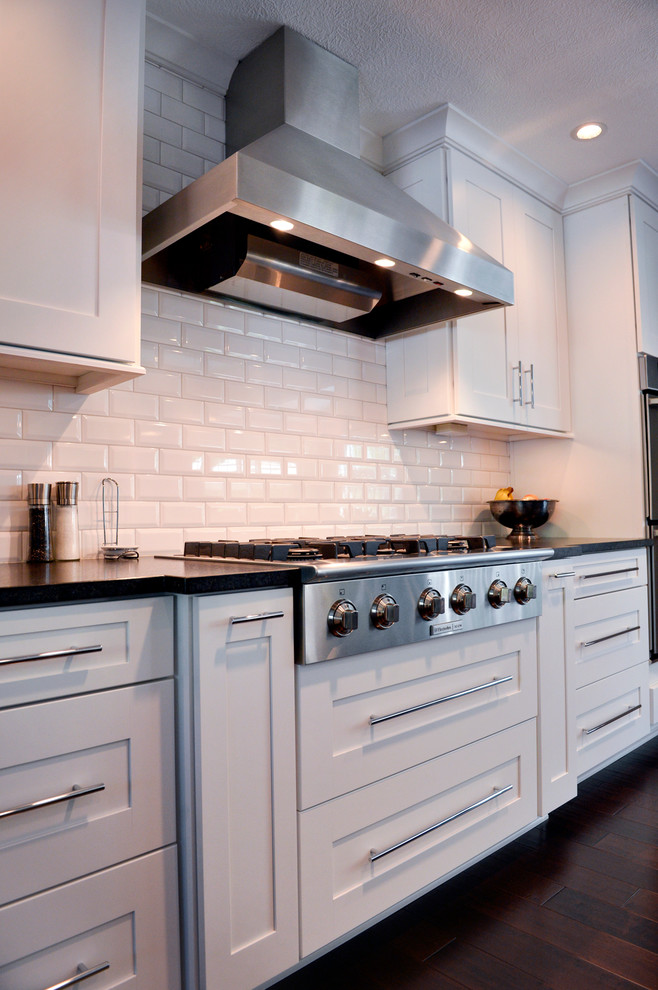 Kitchen - transitional dark wood floor kitchen idea in Cleveland with a drop-in sink, recessed-panel cabinets, white backsplash, ceramic backsplash, stainless steel appliances and an island