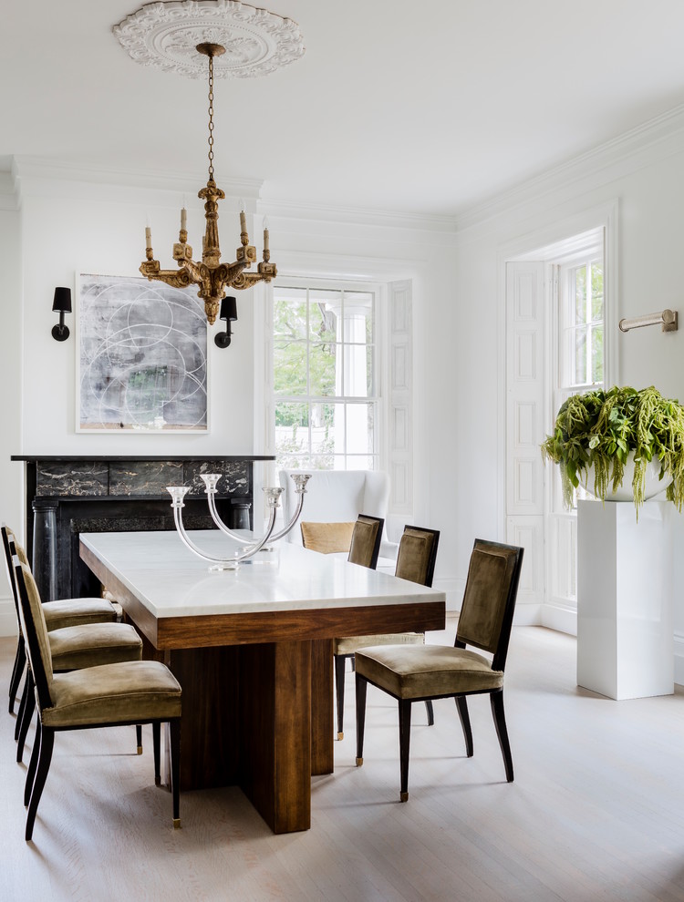 This is an example of a transitional separate dining room with white walls, light hardwood floors, a standard fireplace, a stone fireplace surround and grey floor.