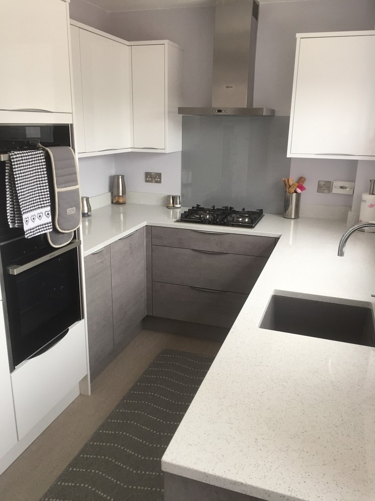 This is an example of a small modern u-shaped separate kitchen in Buckinghamshire with an undermount sink, flat-panel cabinets, white cabinets, quartzite benchtops, grey splashback, glass sheet splashback, panelled appliances, vinyl floors, no island, grey floor and white benchtop.
