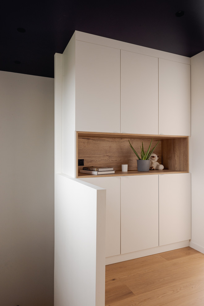 This is an example of a medium sized contemporary gender neutral wardrobe in Paris with flat-panel cabinets, white cabinets, light hardwood flooring and beige floors.