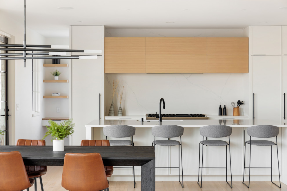 Contemporary kitchen in Minneapolis with white cabinets, quartzite benchtops, stainless steel appliances, light hardwood floors, with island, brown floor and white benchtop.