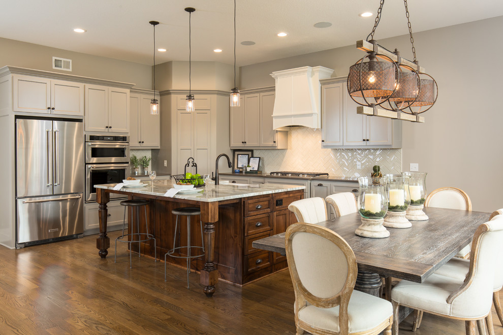 Traditional l-shaped eat-in kitchen in Kansas City with a farmhouse sink, shaker cabinets, white cabinets, white splashback, stainless steel appliances, dark hardwood floors and with island.