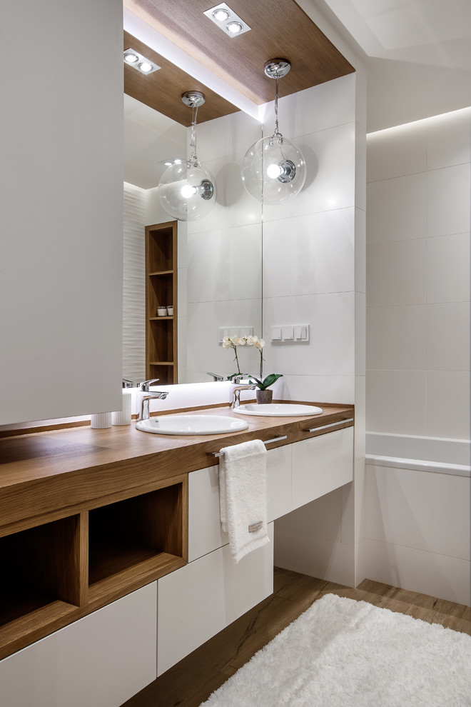Photo of a small contemporary master bathroom in Yekaterinburg with flat-panel cabinets, white cabinets, an alcove tub, a shower/bathtub combo, a wall-mount toilet, white tile, matchstick tile, white walls, porcelain floors, an undermount sink and wood benchtops.