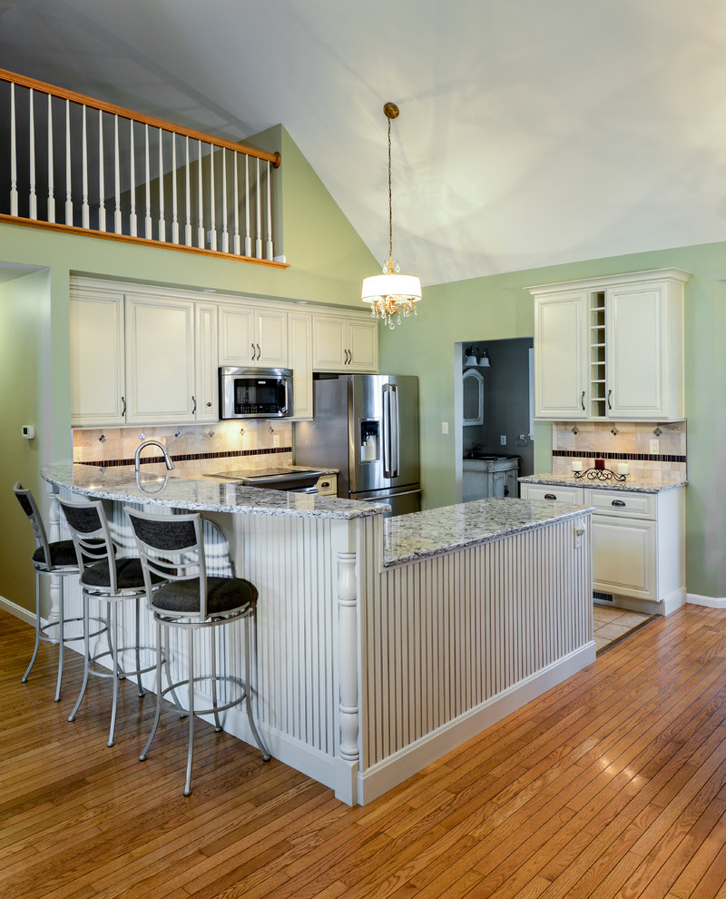 Inspiration for a mid-sized transitional galley open concept kitchen remodel with a double-bowl sink, beaded inset cabinets, white cabinets, wood countertops, beige backsplash, ceramic backsplash, stainless steel appliances and a peninsula