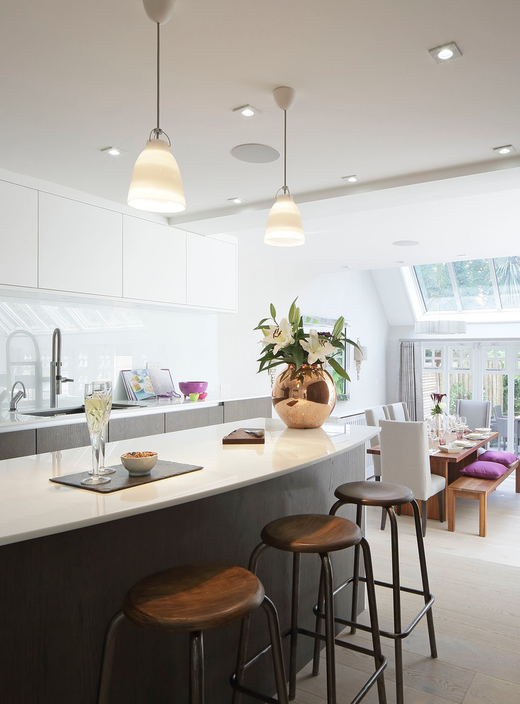 Photo of a contemporary eat-in kitchen in London with flat-panel cabinets, white cabinets, white splashback and with island.