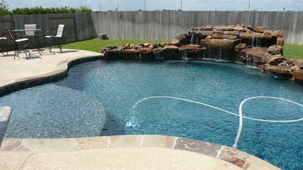 This is an example of a large beach style backyard custom-shaped pool in Houston with a water feature.