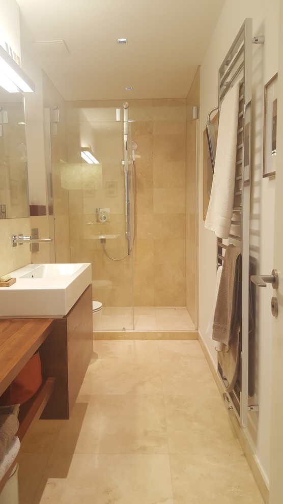 Contemporary 3/4 bathroom in Berlin with flat-panel cabinets, dark wood cabinets, an alcove shower, a wall-mount toilet, beige tile, travertine, beige walls, travertine floors, a wall-mount sink, stainless steel benchtops, beige floor and a sliding shower screen.