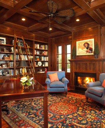 Photo of a mid-sized traditional home office in Charleston with a library, brown walls, dark hardwood floors, a standard fireplace, a freestanding desk and brown floor.