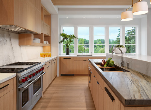 Warm minimalist kitchen cabinet design with light white-oak slab cabinets, stone-veined countertop, marble slab backsplash, and ample natural light from large windows
