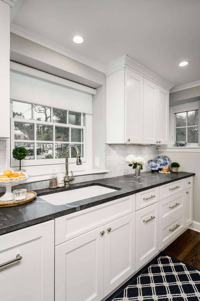 Inspiration for a mid-sized traditional l-shaped eat-in kitchen in Philadelphia with an undermount sink, shaker cabinets, white cabinets, quartz benchtops, white splashback, porcelain splashback, stainless steel appliances, medium hardwood floors, with island, brown floor and black benchtop.