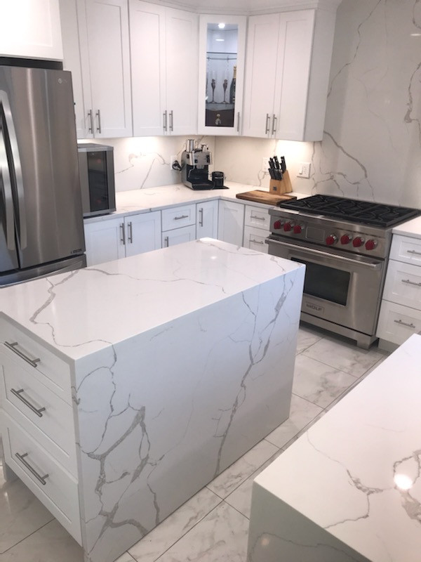 Photo of a mid-sized modern u-shaped separate kitchen in New York with shaker cabinets, white cabinets, quartz benchtops, white splashback, stone slab splashback, stainless steel appliances, with island, white benchtop, a farmhouse sink, porcelain floors and multi-coloured floor.