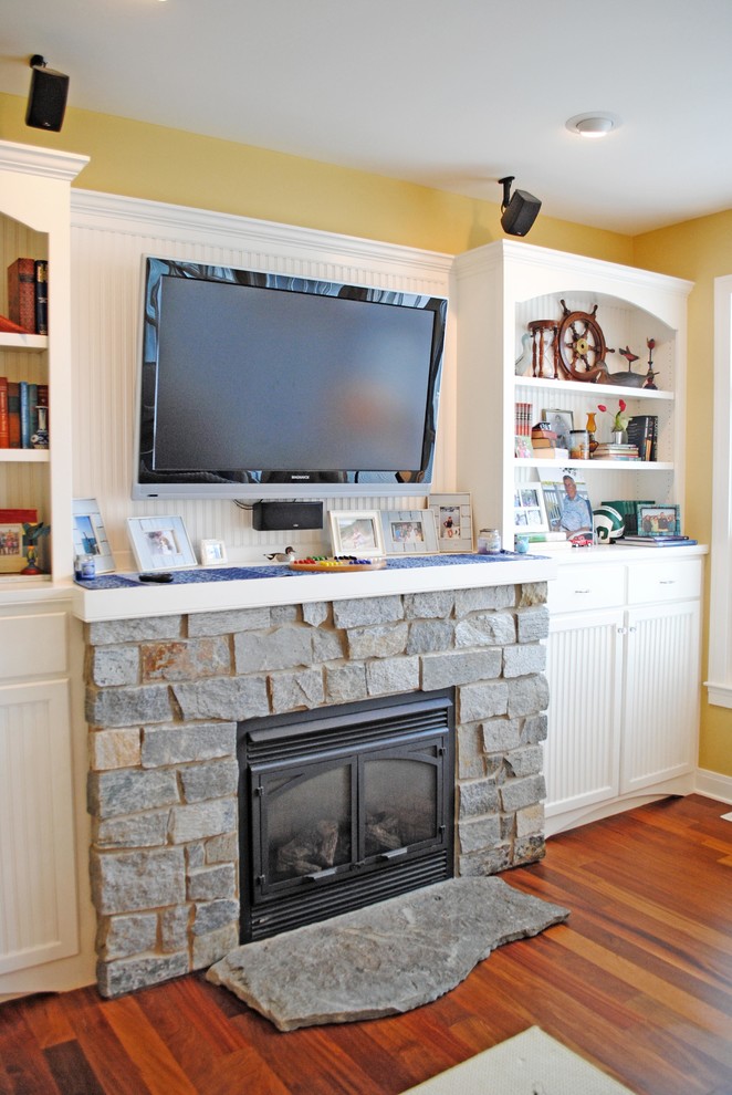 This is an example of a large beach style open concept family room in Grand Rapids with yellow walls, medium hardwood floors, a standard fireplace, a stone fireplace surround and a built-in media wall.