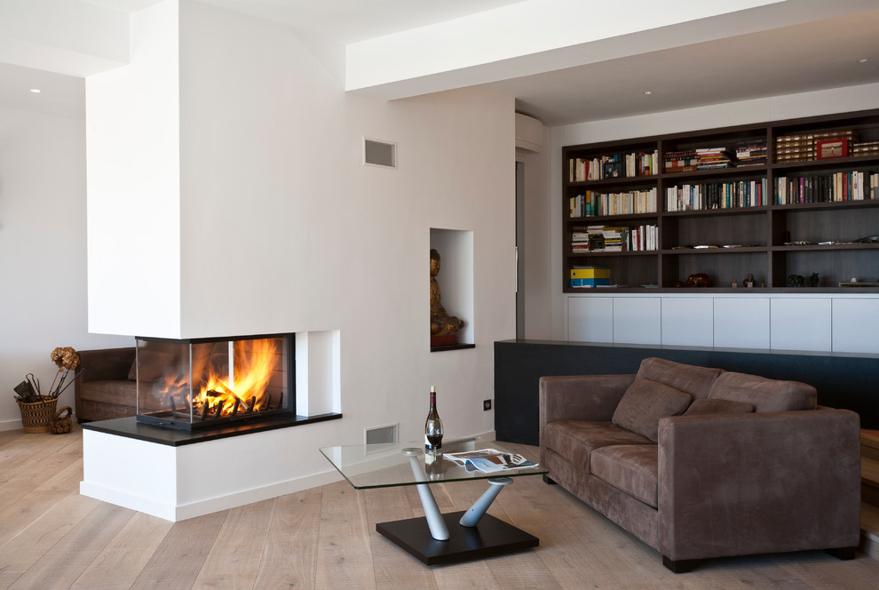 Inspiration for a mid-sized contemporary open concept living room in Montpellier with a library, white walls, light hardwood floors, a two-sided fireplace, a plaster fireplace surround and no tv.