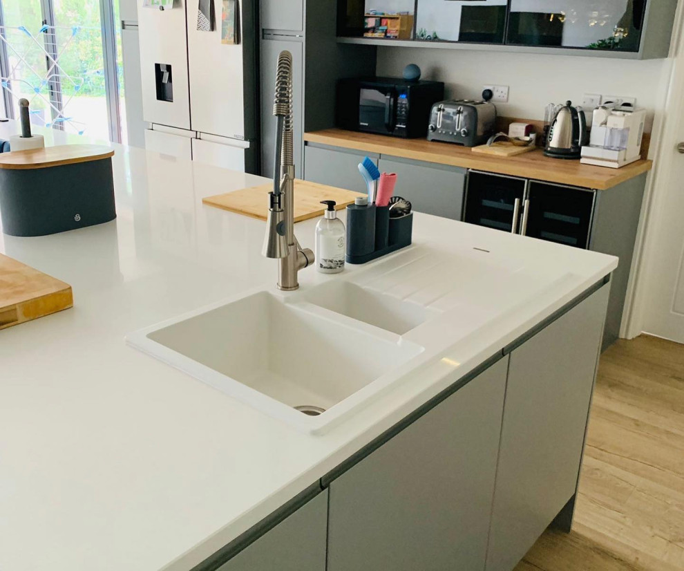 This is an example of a large modern single-wall open plan kitchen in Other with a double-bowl sink, flat-panel cabinets, grey cabinets, quartzite benchtops, black splashback, glass sheet splashback, black appliances, vinyl floors, with island, brown floor and white benchtop.