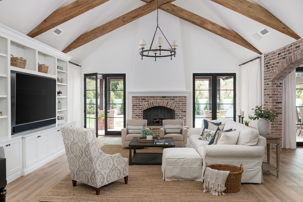 Photo of a large country open concept family room in Phoenix with white walls, medium hardwood floors, a standard fireplace, a brick fireplace surround, a built-in media wall and beige floor.