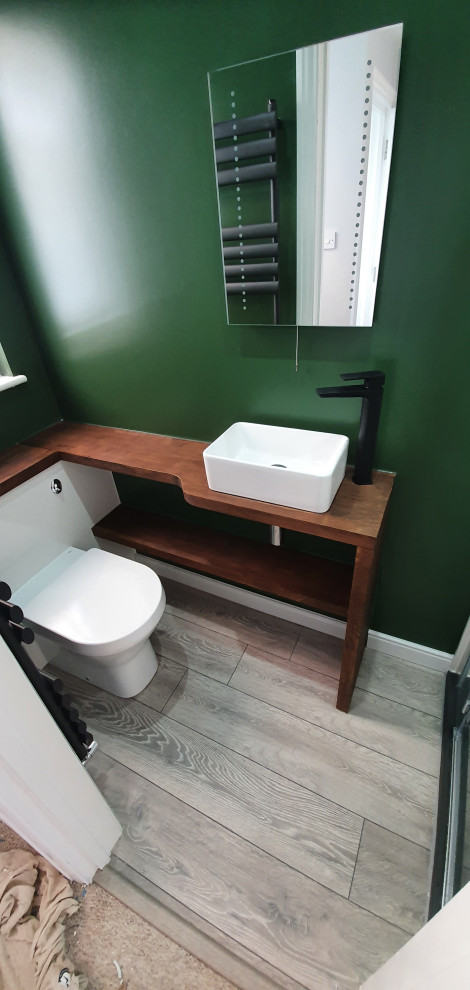 Inspiration for a small contemporary bathroom in Surrey with flat-panel cabinets, white cabinets, an open shower, a one-piece toilet, green walls, laminate floors, a trough sink, wood benchtops, grey floor, a hinged shower door, brown benchtops, a single vanity and a built-in vanity.