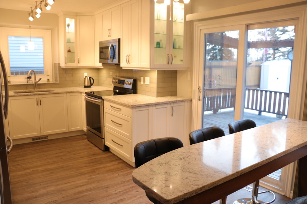 Inspiration for a small transitional u-shaped eat-in kitchen remodel in Edmonton with an undermount sink, recessed-panel cabinets, white cabinets, quartz countertops, gray backsplash, glass tile backsplash, stainless steel appliances, no island and white countertops