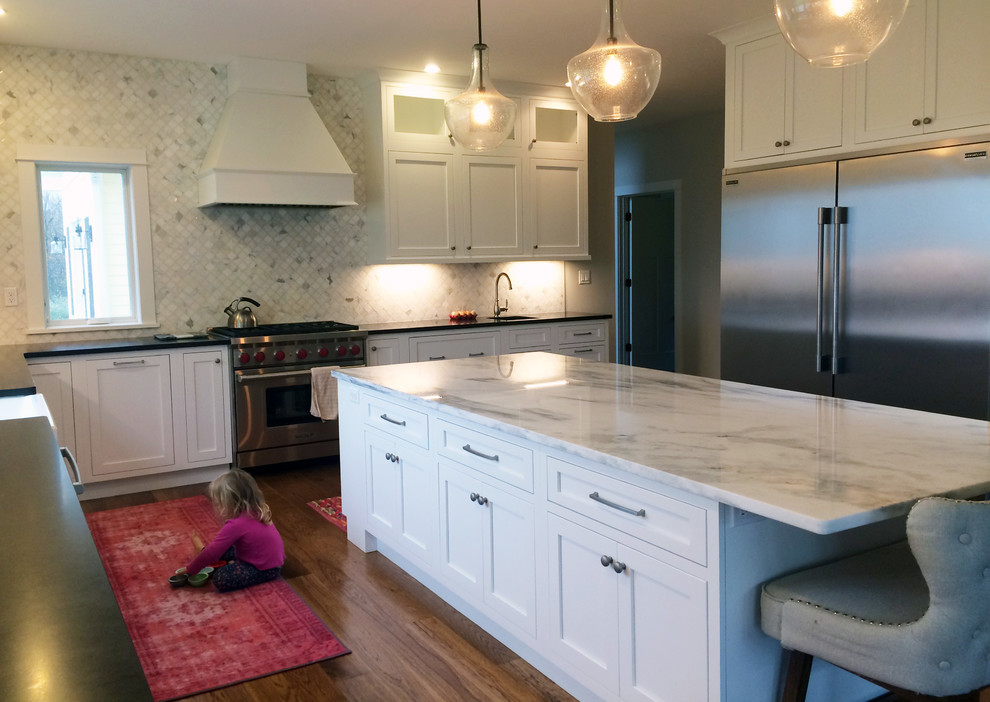 Example of a large transitional u-shaped kitchen pantry design with a farmhouse sink, recessed-panel cabinets, white cabinets, quartzite countertops, stainless steel appliances, an island and black countertops