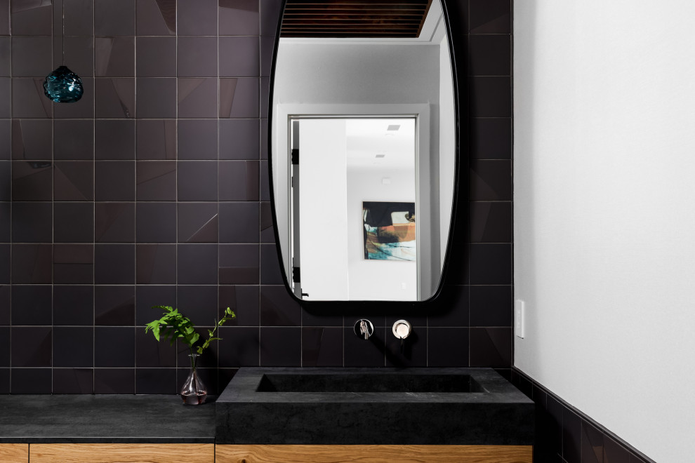 This is an example of a large modern powder room in Austin with flat-panel cabinets, a one-piece toilet, porcelain floors, white benchtops, a floating vanity, recessed, panelled walls, black cabinets, black tile, ceramic tile, black walls, an integrated sink, concrete benchtops and brown floor.