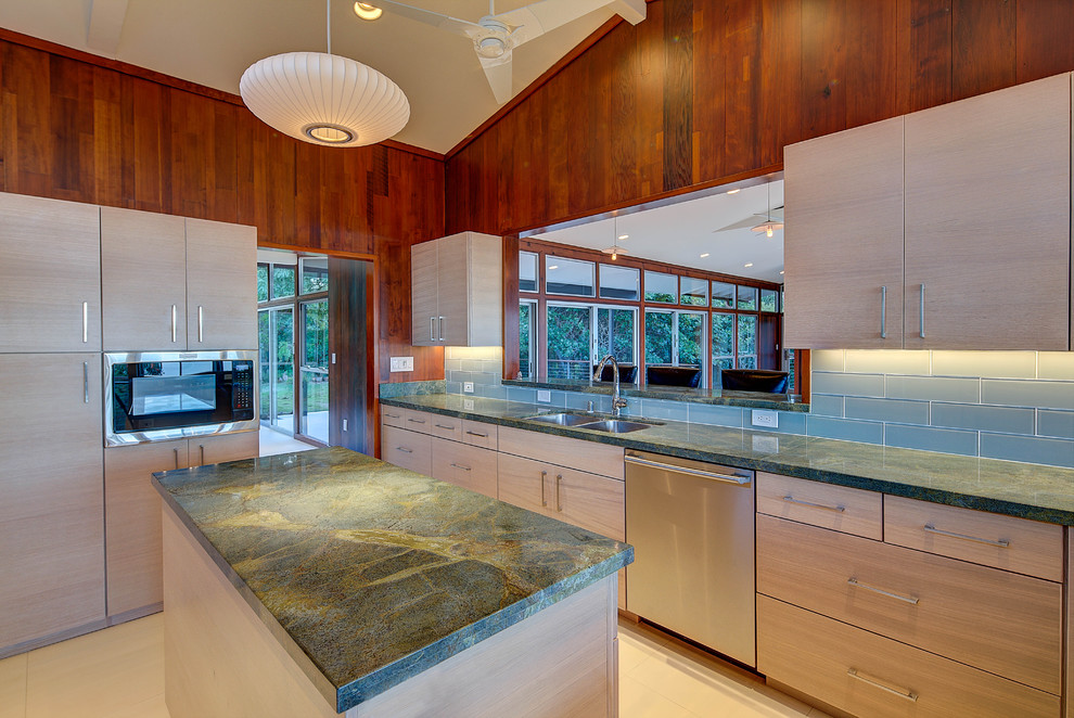 This is an example of a mid-sized midcentury u-shaped kitchen in Hawaii with an undermount sink, flat-panel cabinets, light wood cabinets, granite benchtops, blue splashback, glass tile splashback, stainless steel appliances, porcelain floors and with island.
