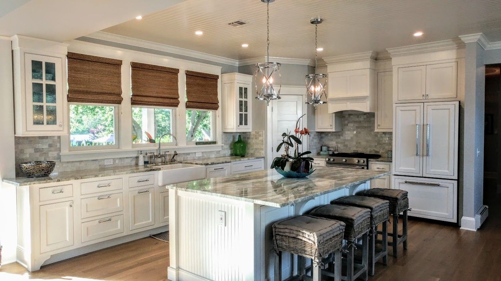 Example of a large transitional l-shaped medium tone wood floor and brown floor open concept kitchen design with a farmhouse sink, recessed-panel cabinets, white cabinets, granite countertops, gray backsplash, stone tile backsplash, paneled appliances, an island and gray countertops