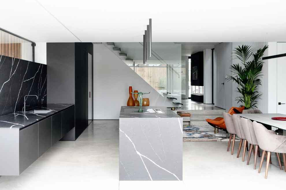 Ispirazione per una cucina minimalista con lavello sottopiano, ante lisce, ante grigie, paraspruzzi nero, paraspruzzi in lastra di pietra, pavimento in cemento, pavimento grigio e top nero