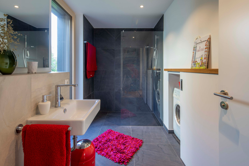 Skandinavisches Badezimmer mit bodengleicher Dusche, grauen Fliesen, Wandwaschbecken, grauem Boden und offener Dusche in München