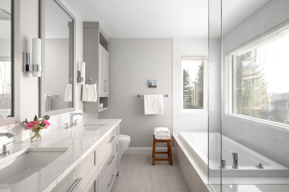 Inspiration for a mid-sized transitional master bathroom in Calgary with grey cabinets, a drop-in tub, grey walls, an undermount sink, beige floor, white benchtops, ceramic tile, engineered quartz benchtops, a hinged shower door and recessed-panel cabinets.