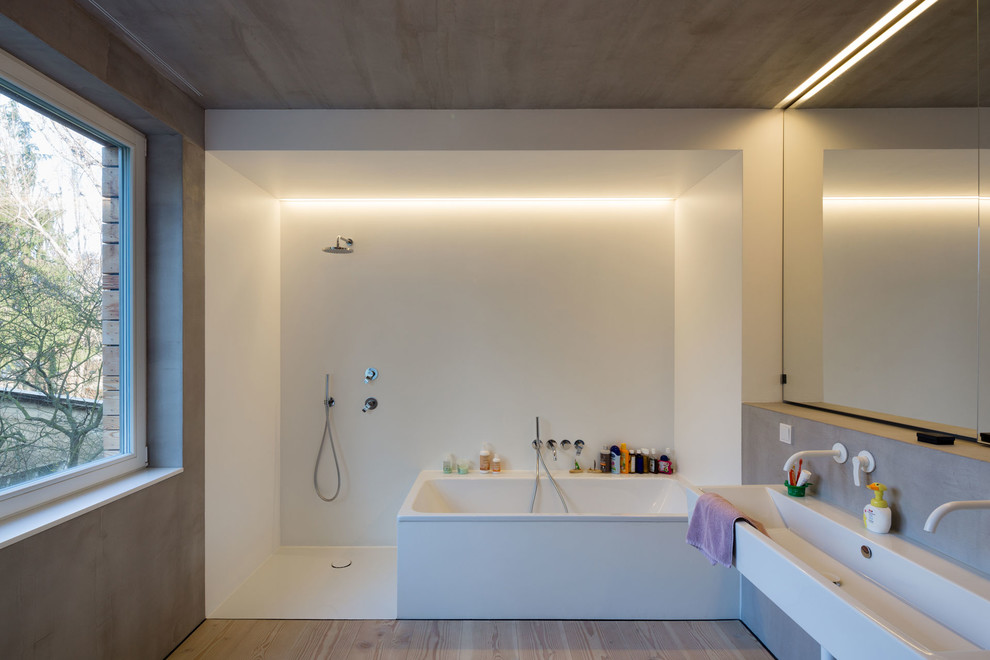 Photo of a mid-sized contemporary 3/4 bathroom in Berlin with an alcove tub, an open shower, white walls, light hardwood floors, a trough sink, a wall-mount toilet, an open shower, beige floor, a single vanity and a floating vanity.