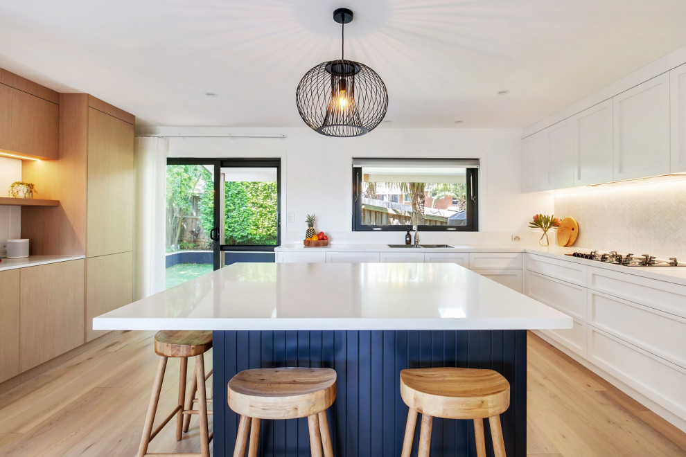 Inspiration for a large beach style l-shaped kitchen pantry in Sydney with a double-bowl sink, shaker cabinets, blue cabinets, quartz benchtops, white splashback, mosaic tile splashback, stainless steel appliances, light hardwood floors, with island, multi-coloured floor, white benchtop and recessed.