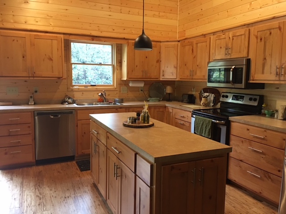 Large mountain style l-shaped medium tone wood floor and brown floor kitchen photo with a double-bowl sink, shaker cabinets, light wood cabinets, solid surface countertops, brown backsplash, wood backsplash and stainless steel appliances