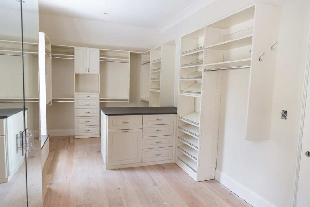 Photo of a large transitional gender-neutral walk-in wardrobe in Atlanta with raised-panel cabinets, white cabinets and light hardwood floors.