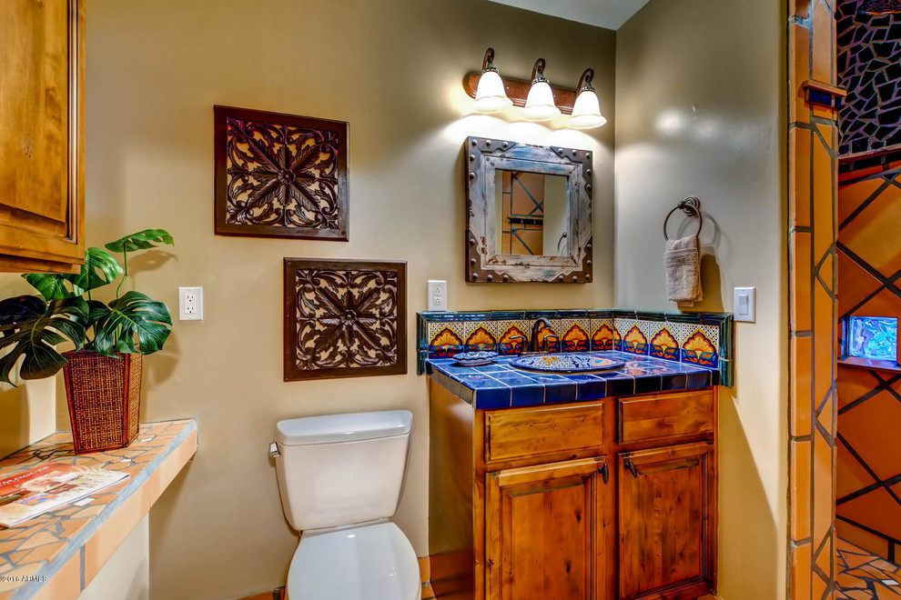 Photo of a mid-sized 3/4 bathroom in Phoenix with raised-panel cabinets, dark wood cabinets, a corner shower, a two-piece toilet, orange tile, terra-cotta tile, beige walls, terra-cotta floors, a drop-in sink, tile benchtops, an open shower and blue benchtops.