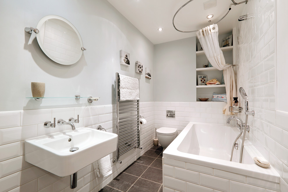 Inspiration for a small scandinavian kids bathroom in Sussex with open cabinets, a drop-in tub, a wall-mount toilet, white tile, subway tile, a wall-mount sink, a shower/bathtub combo, ceramic floors, white cabinets, blue walls and a shower curtain.