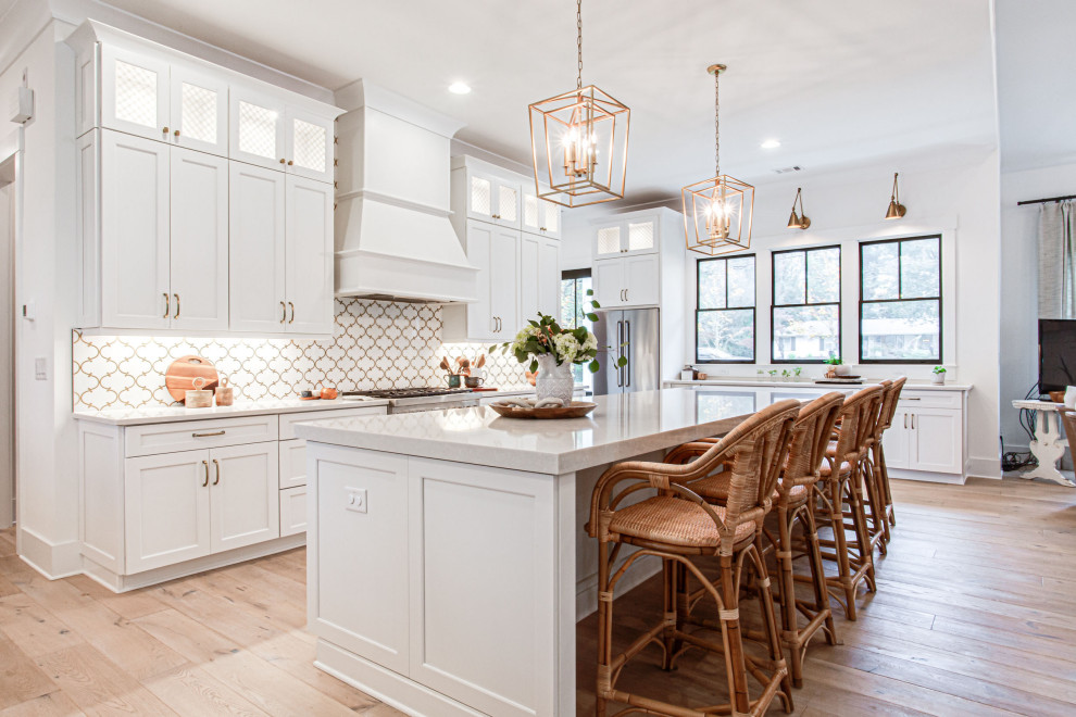 Photo of a large farmhouse u-shaped open plan kitchen in Atlanta with a belfast sink, shaker cabinets, white cabinets, engineered stone countertops, white splashback, mosaic tiled splashback, stainless steel appliances, light hardwood flooring, an island, beige floors, grey worktops and a vaulted ceiling.
