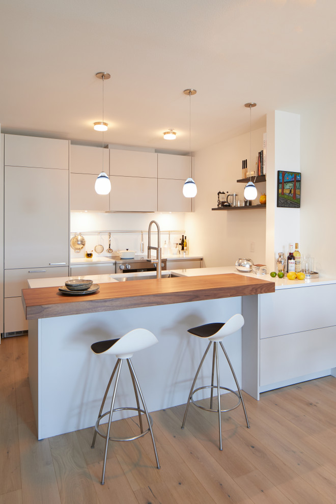 Inspiration for a contemporary eat-in kitchen in Seattle with an undermount sink, flat-panel cabinets, white cabinets, quartz benchtops, white splashback, engineered quartz splashback, panelled appliances, light hardwood floors, a peninsula, beige floor and white benchtop.