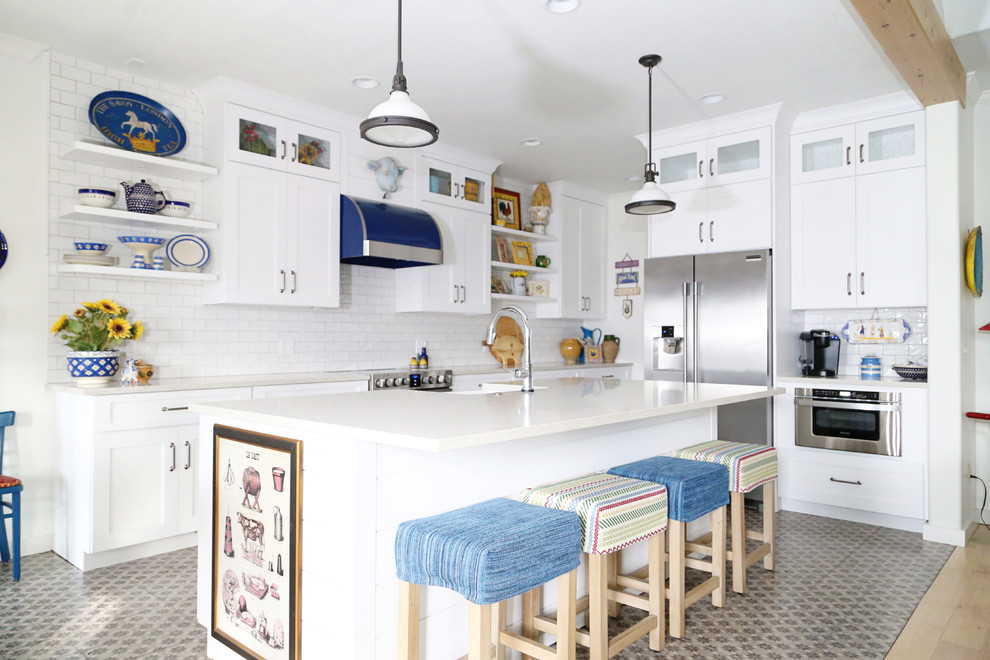 This is an example of a country l-shaped open plan kitchen in Other with a farmhouse sink, shaker cabinets, white cabinets, white splashback, subway tile splashback, stainless steel appliances, with island and multi-coloured floor.