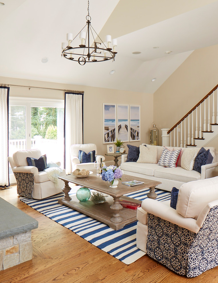 This is an example of a mid-sized beach style open concept family room in Boston with beige walls, medium hardwood floors, a standard fireplace, a stone fireplace surround and brown floor.