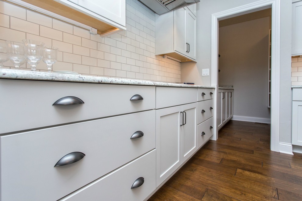 Open concept kitchen - mid-sized transitional single-wall medium tone wood floor and beige floor open concept kitchen idea with a farmhouse sink, recessed-panel cabinets, white cabinets, granite countertops, white backsplash, ceramic backsplash, stainless steel appliances and an island