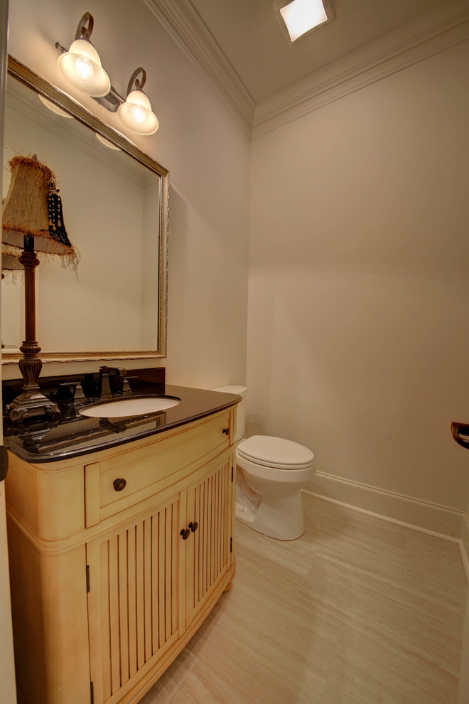 Mid-sized traditional powder room in New Orleans with furniture-like cabinets, yellow cabinets, a one-piece toilet, white walls, light hardwood floors and an undermount sink.