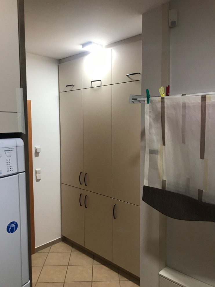 Multifunktionaler, Mittelgroßer Moderner Hauswirtschaftsraum mit Ausgussbecken, flächenbündigen Schrankfronten, beigen Schränken, Laminat-Arbeitsplatte, weißer Wandfarbe, Keramikboden, Waschmaschine und Trockner gestapelt, beigem Boden und brauner Arbeitsplatte in Berlin