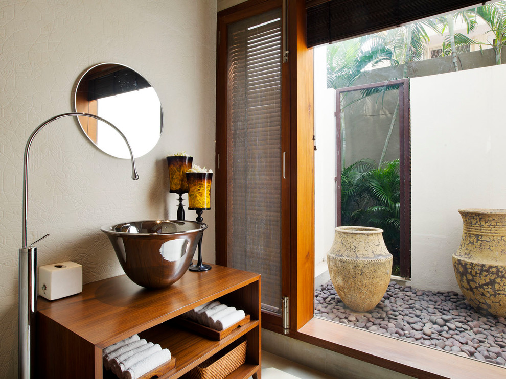 This is an example of a tropical powder room in Bengaluru with open cabinets, medium wood cabinets, beige walls, a vessel sink, wood benchtops and brown benchtops.