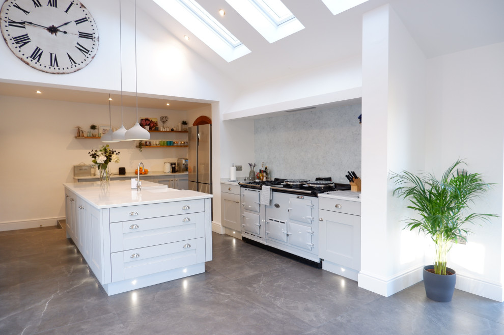Photo of a large contemporary open plan kitchen in Other with a farmhouse sink, shaker cabinets, grey cabinets, quartzite benchtops, glass sheet splashback, coloured appliances, with island, grey floor and white benchtop.