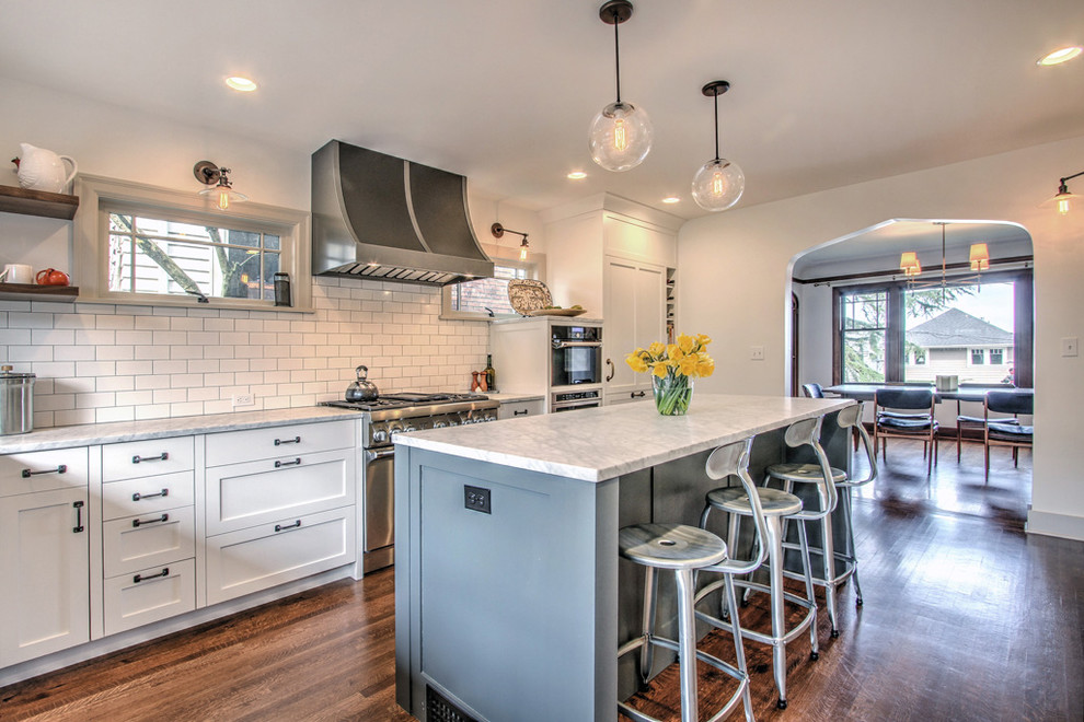 This is an example of a traditional kitchen in Seattle with shaker cabinets, white cabinets, white splashback, subway tile splashback, stainless steel appliances, dark hardwood floors and with island.