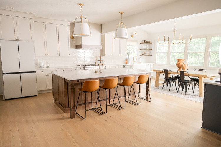 Large transitional u-shaped light wood floor, brown floor and vaulted ceiling eat-in kitchen photo with an undermount sink, shaker cabinets, white cabinets, quartz countertops, white backsplash, porcelain backsplash, stainless steel appliances, an island and white countertops